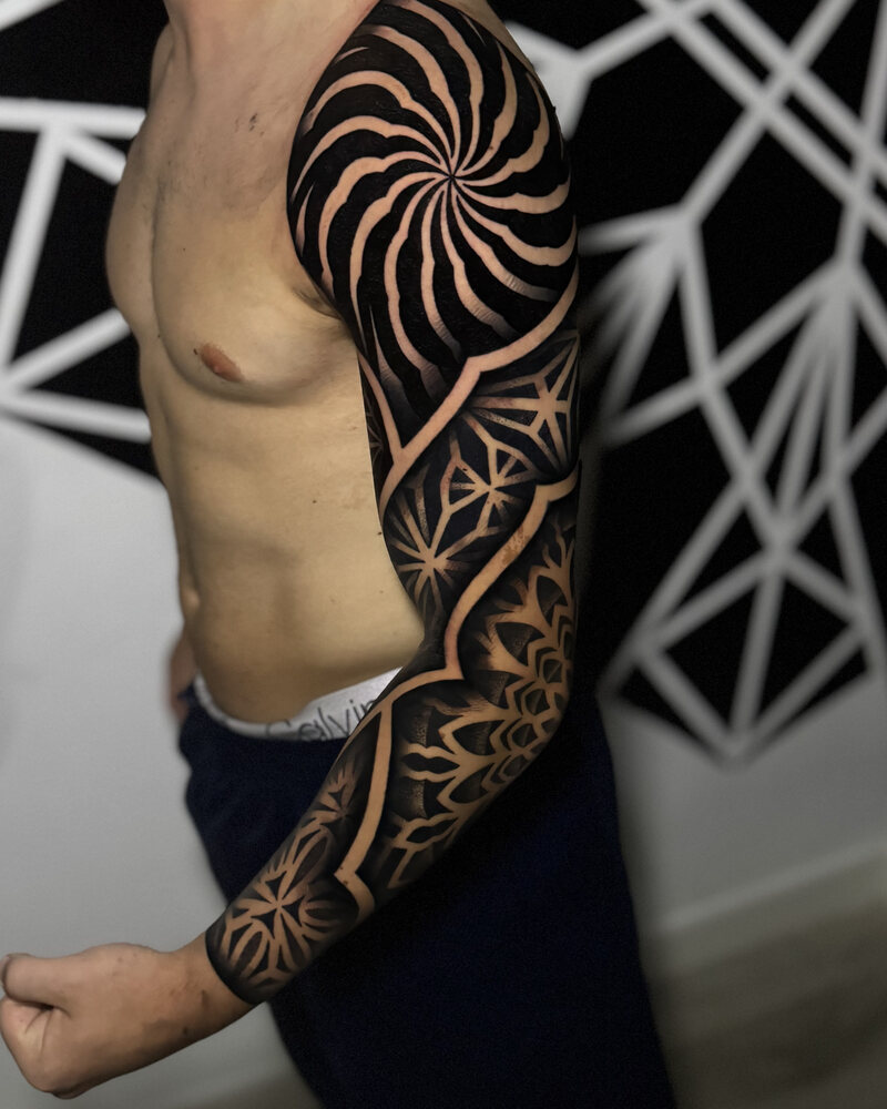 Tatuaje blackout de manga con una espiral radial en el hombro y geometría en el brazo, en negro
